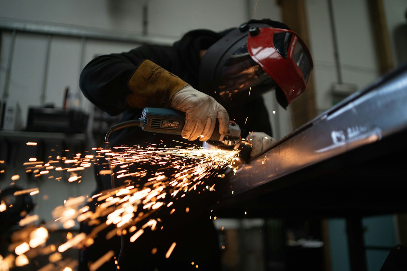Worker in a welding helmet grinding a steel beam with sparks